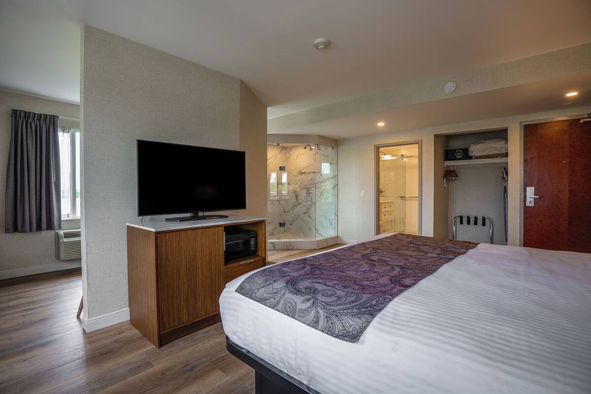 Une chambre d’hôtel moderne dotée d’un grand lit, d’une télévision à écran plat, d’un dressing et d’un espace douche.