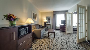 Een hotelkamer met een kitchenette, een bank, een bureau, een lamp en een grote spiegel.