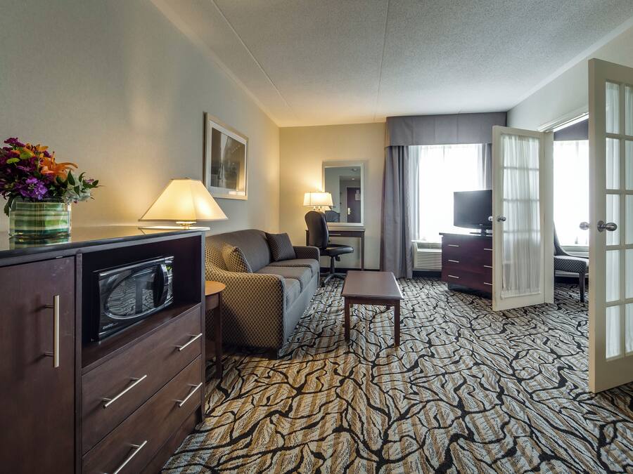 Een hotelkamer met een kitchenette, een bank, een bureau, een lamp en een grote spiegel.