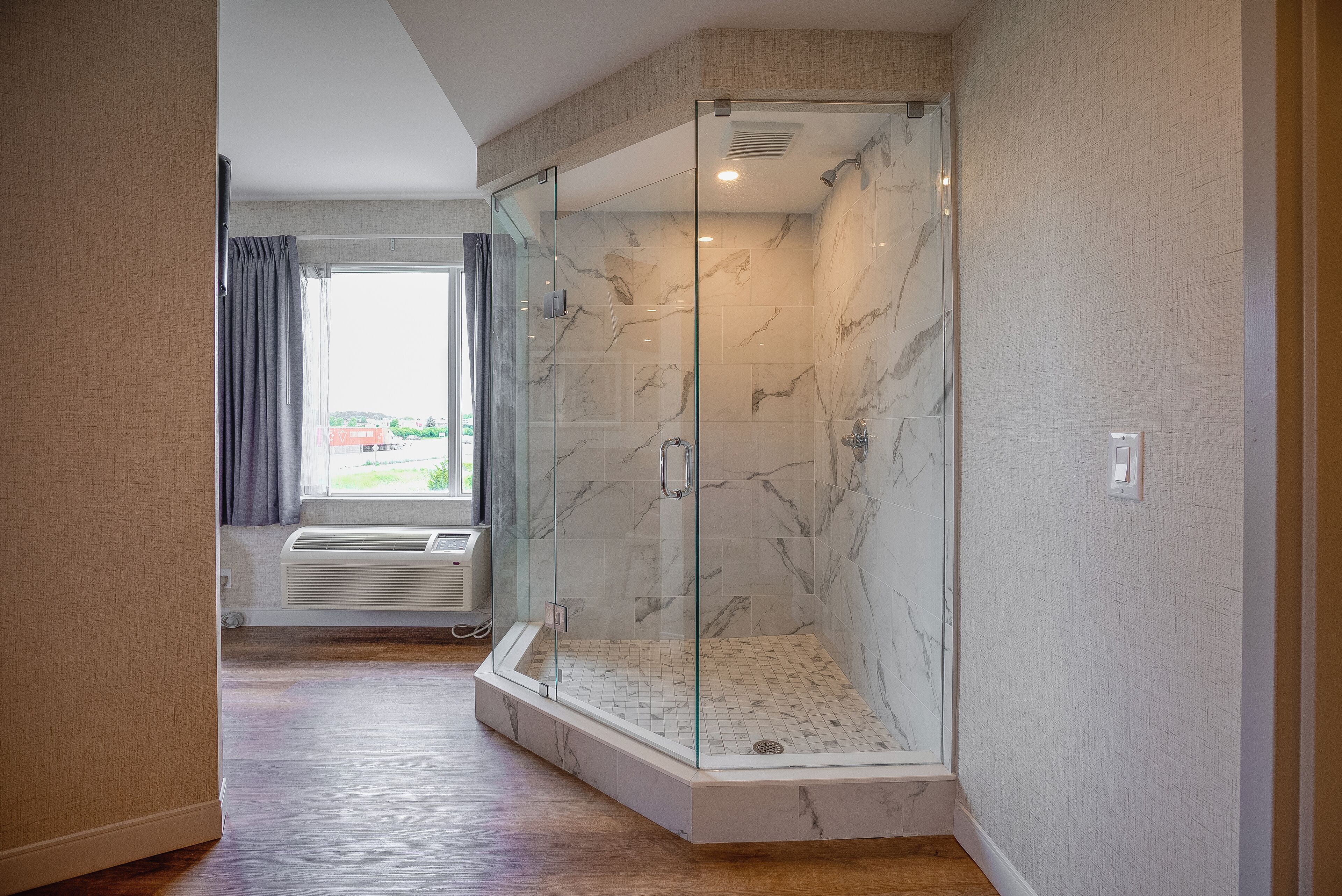A modern bathroom with a glass-enclosed shower, marble walls, and a window with curtains.