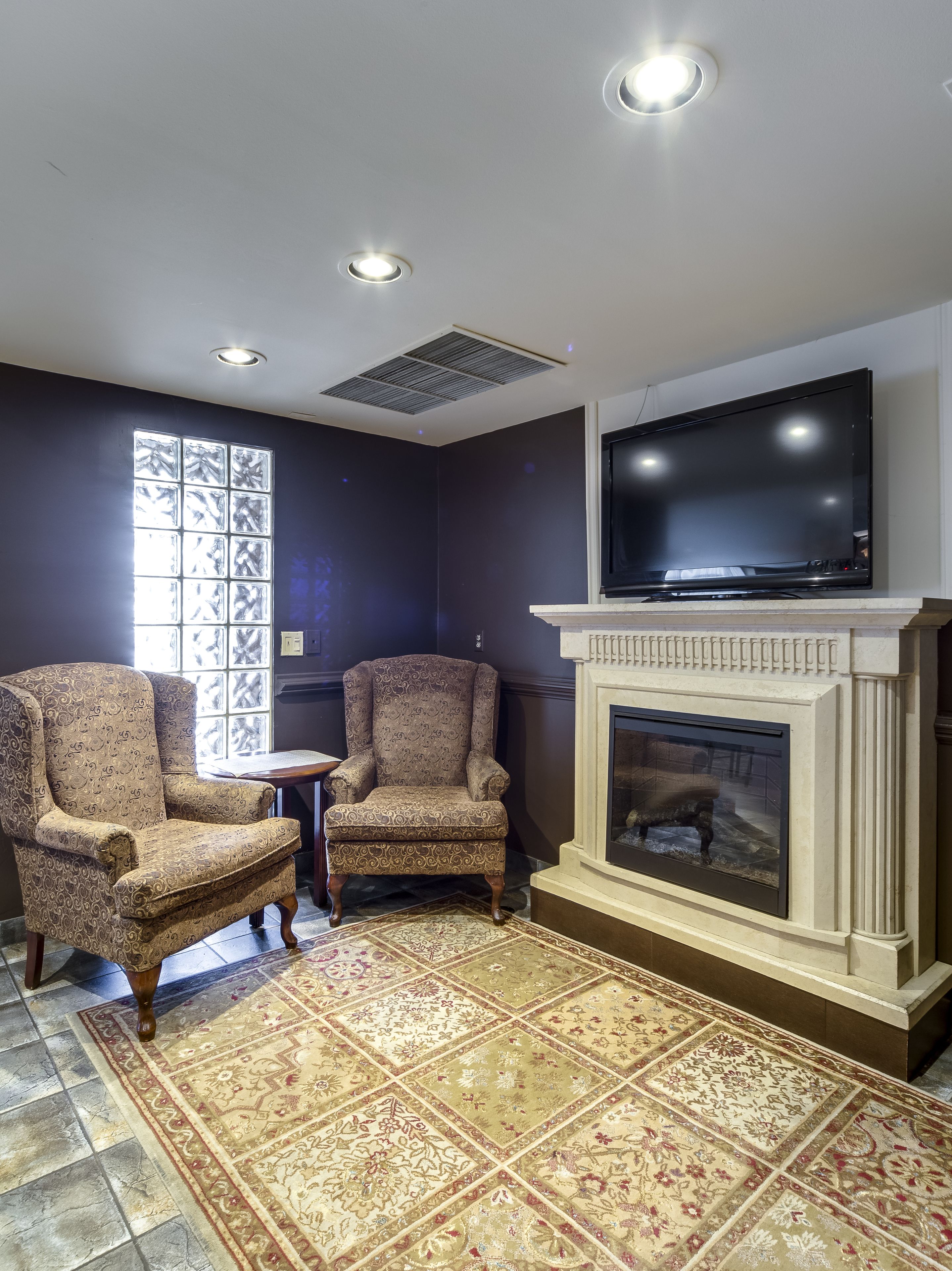 A living room with two armchairs, a television, a fireplace, and a patterned rug.