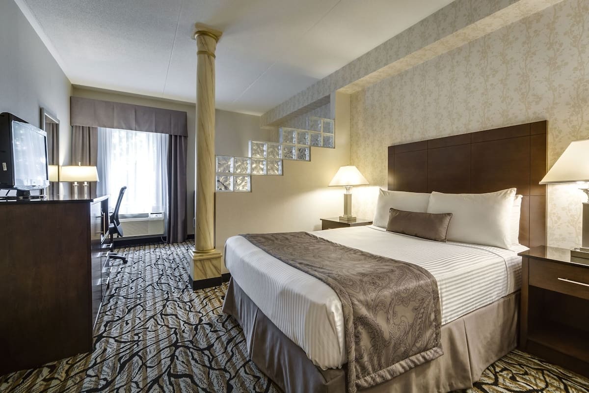 Une chambre d’hôtel avec un lit, deux lampes de chevet, une télévision, un bureau et une moquette à motifs.