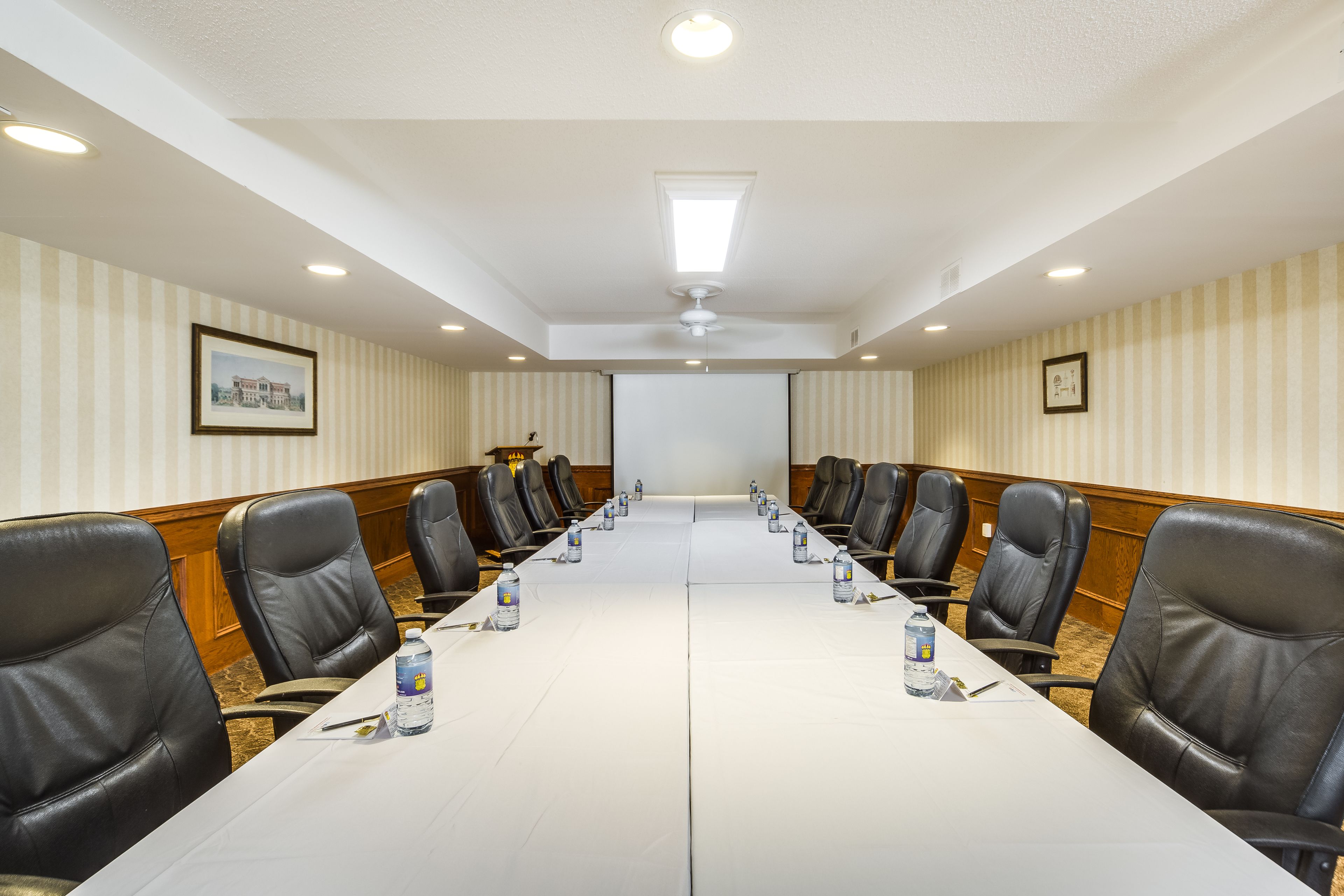Een vergaderruimte met een lange tafel, zwarte lederen stoelen en een scherm voor een projector.