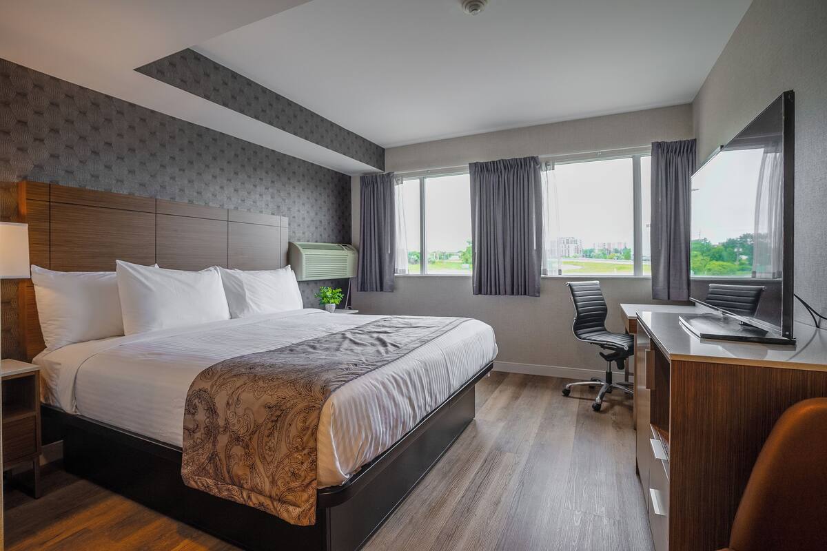 Une chambre d’hôtel avec un grand lit, un bureau et une chaise. Il y a une fenêtre avec des rideaux et une vue sur l’extérieur.