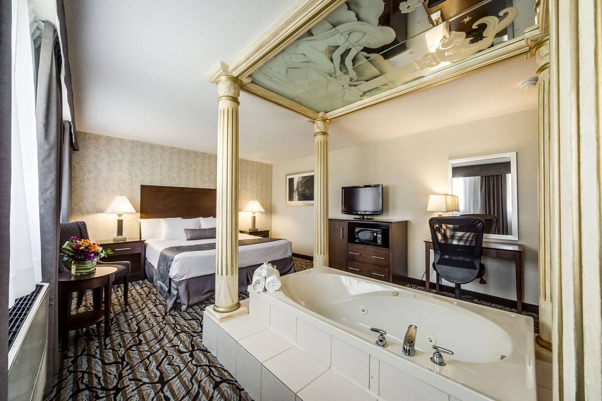 Une chambre d’hôtel avec une grande baignoire, un lit avec une tête de lit, un bureau avec une chaise, une télévision et un miroir.