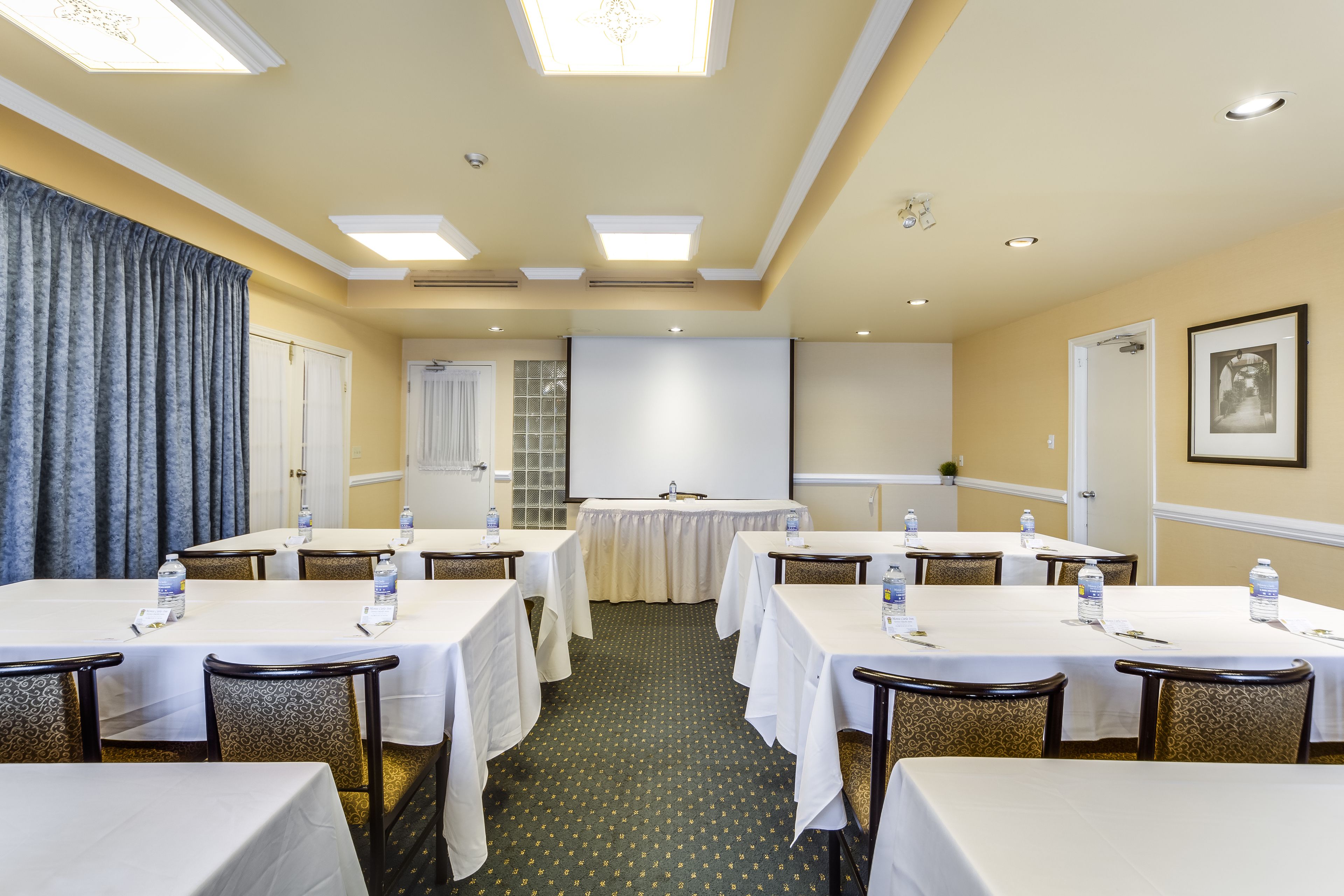Un salón de conferencias con mesas, sillas y una pantalla para proyector.