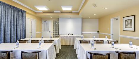 Un salón de conferencias con mesas, sillas y una pantalla para proyector.