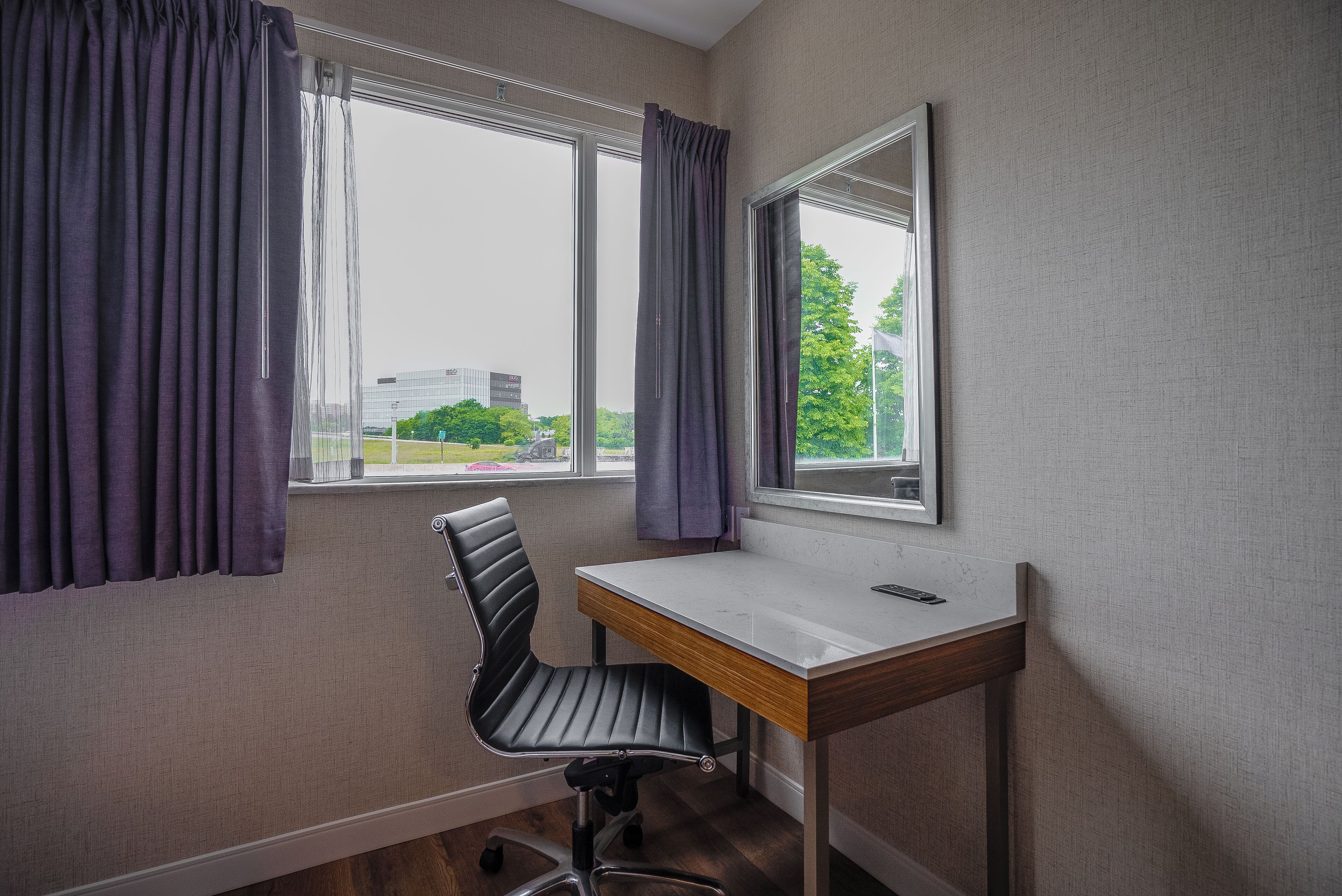 A room with a desk, chair, and large windows with curtains.
