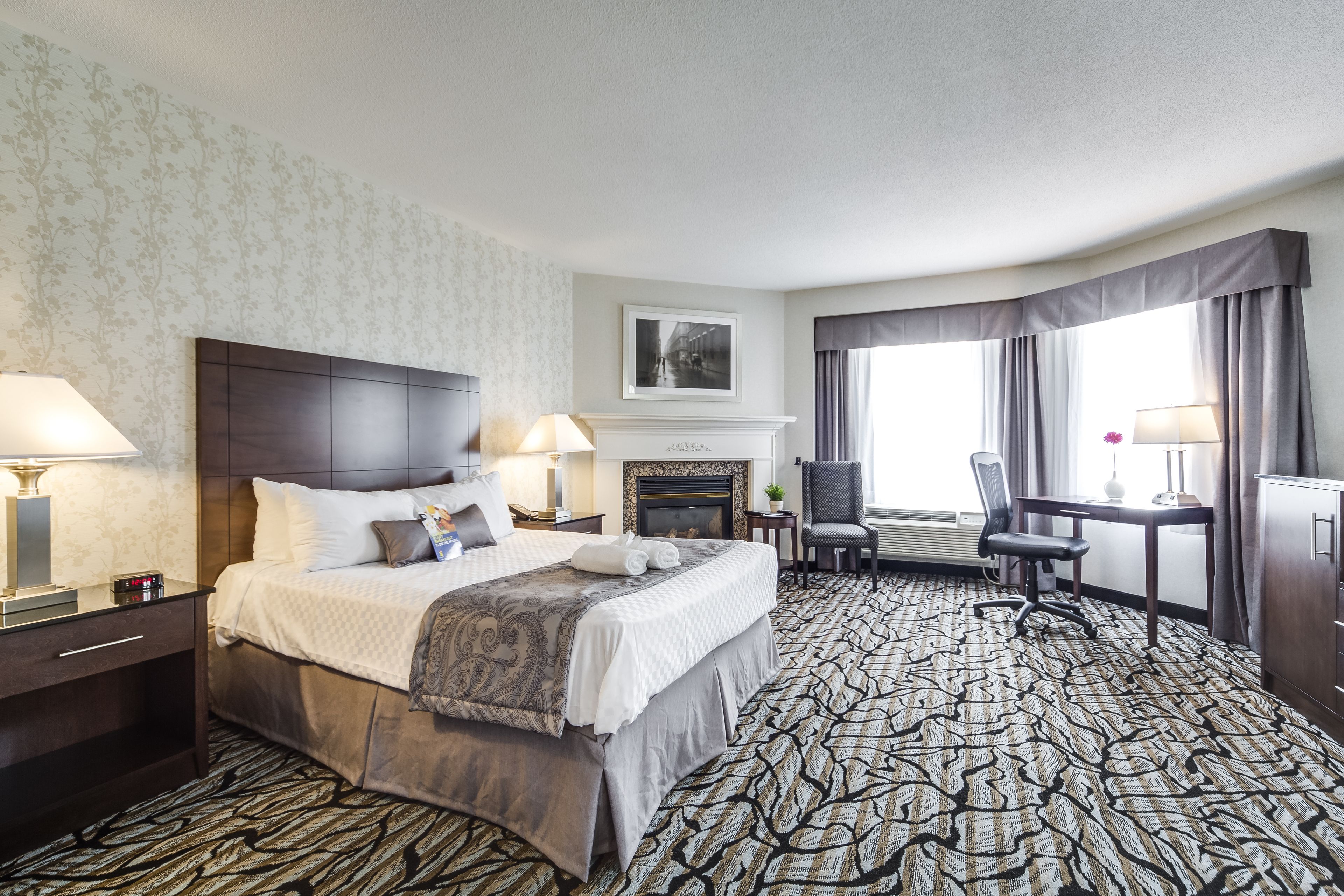 Een hotelkamer met een groot bed, een open haard, een bureau en een stoel.