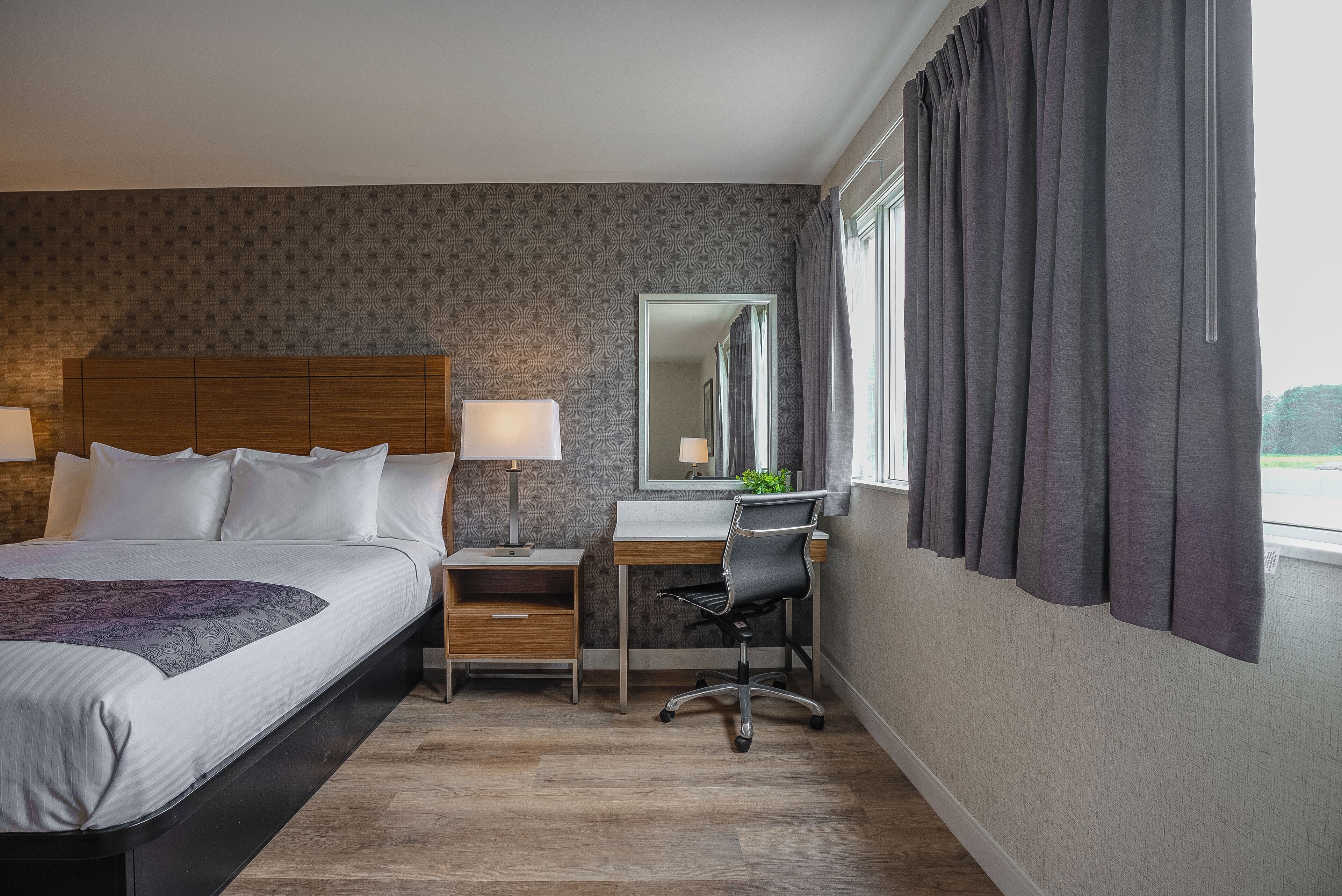 A hotel room with a bed, desk, chair, and a large window with curtains.