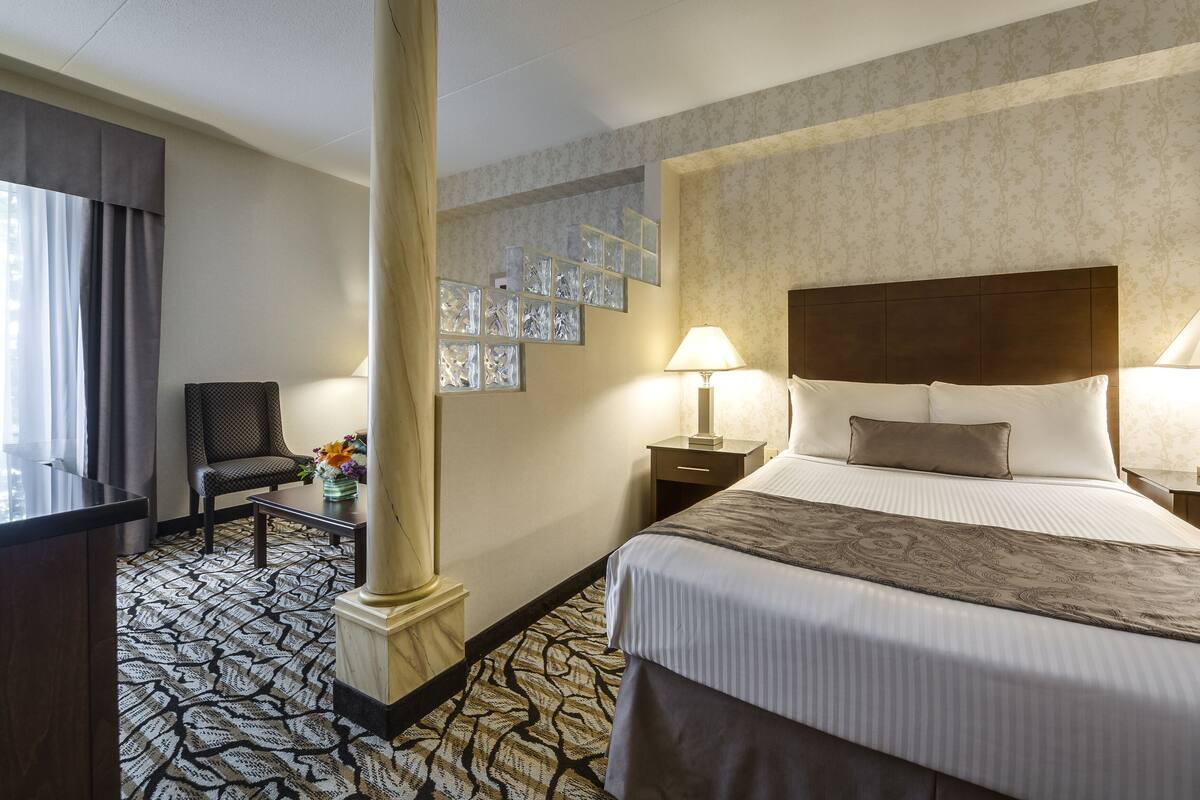 Une chambre d’hôtel comprenant un lit, deux tables de chevet avec des lampes, une chaise, un bureau et un tapis à motifs.
