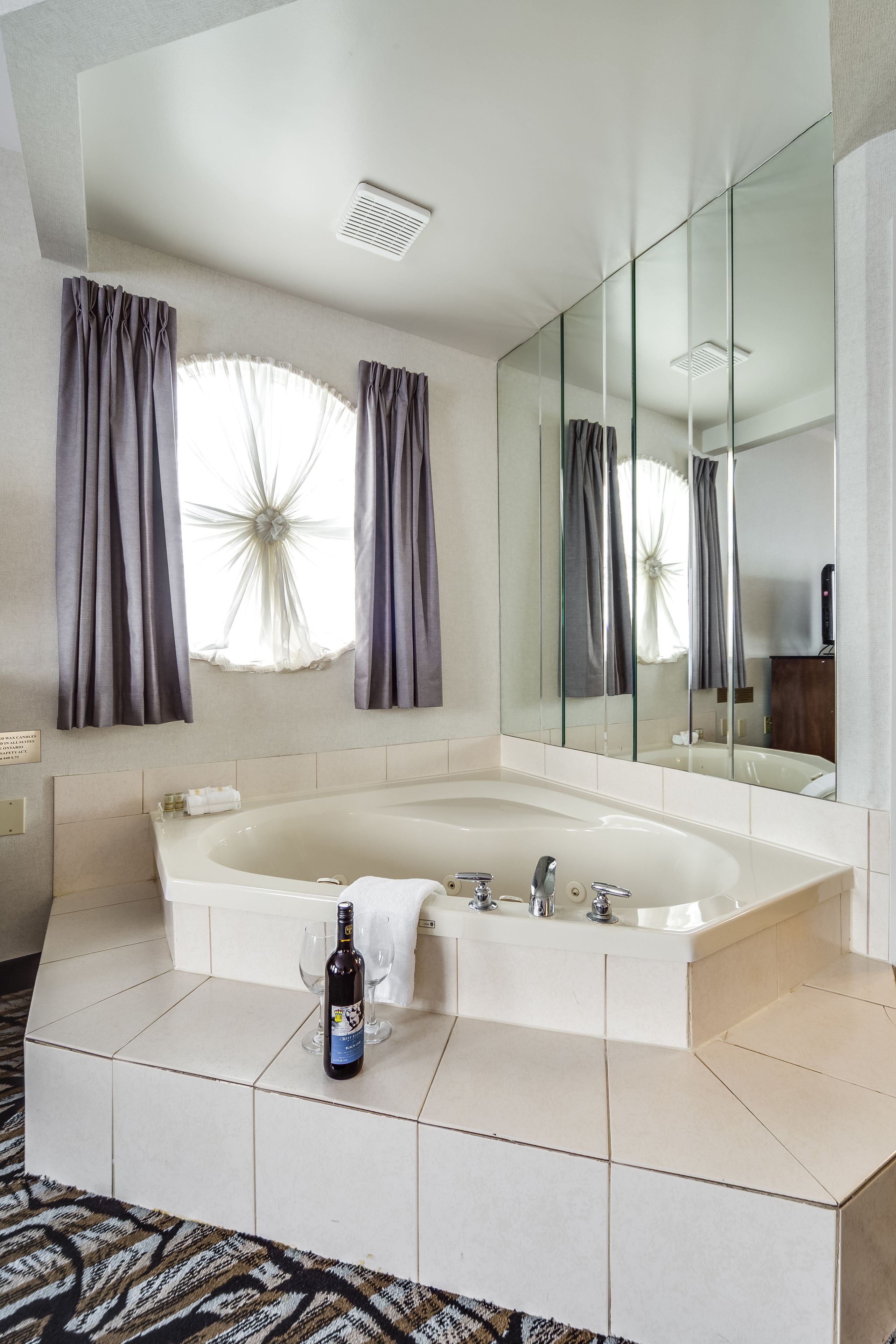 Une salle de bain moderne avec une grande baignoire, un miroir et une fenêtre avec des rideaux.