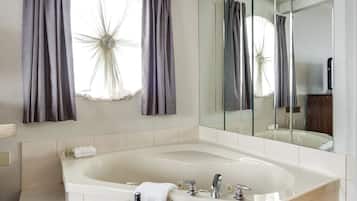 Une salle de bain moderne avec une grande baignoire, un miroir et une fenêtre avec des rideaux.