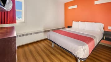 Una habitación de hotel con cama, cómoda de madera, ventana con cortinas y calefacción en la pared.