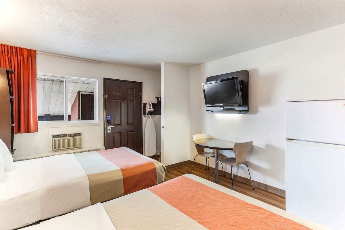 Habitación de hotel con dos camas, televisor, escritorio y una silla.
