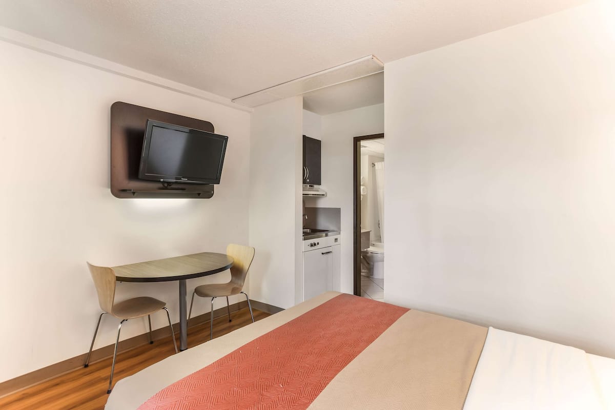 Habitación de hotel con cama, televisión montada en la pared, una pequeña mesa de comedor y sillas.