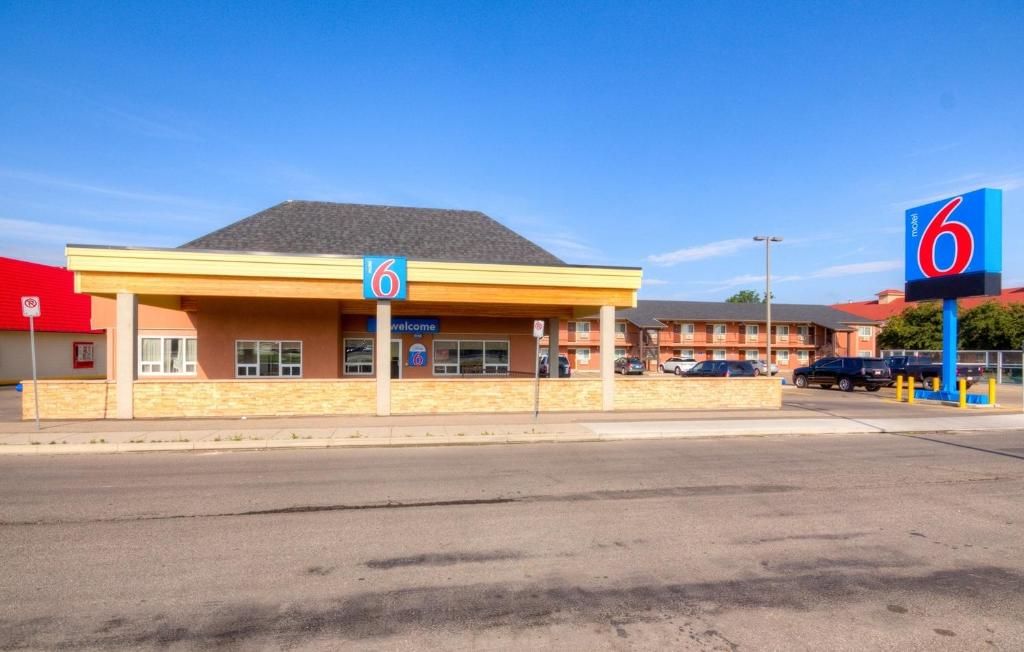Motel 6 con una estructura de un solo nivel, estacionamiento y un cielo azul despejado.