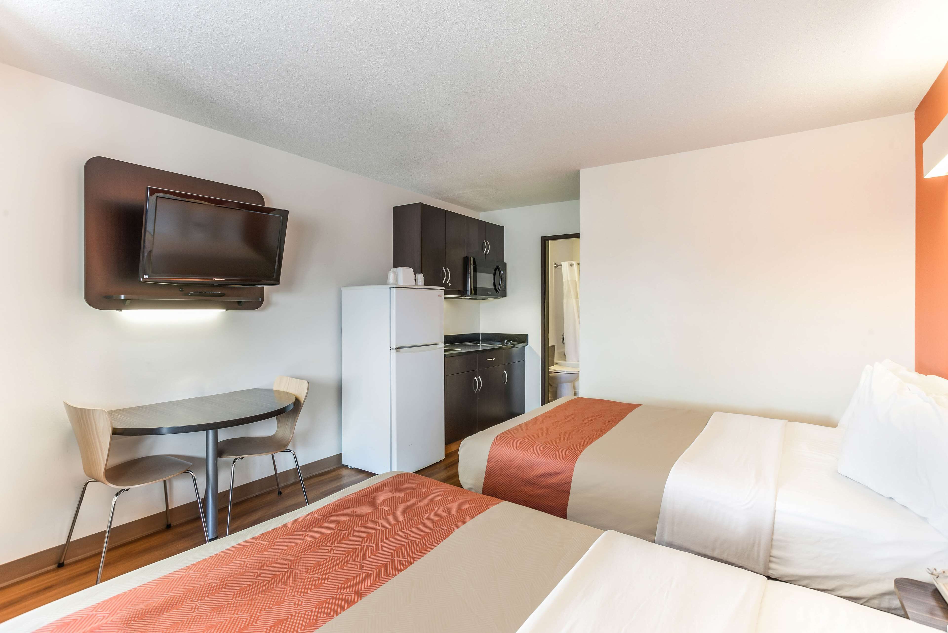 A hotel room with two beds, a small desk, a refrigerator, a microwave, and a television mounted on the wall.