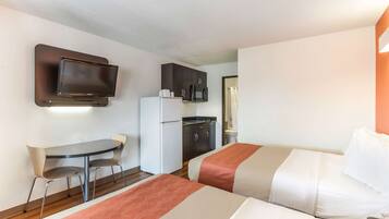A hotel room with two beds, a small desk, a refrigerator, a microwave, and a television mounted on the wall.