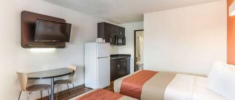 Habitación de hotel con dos camas, un escritorio pequeño, refrigerador, microondas y televisor montado en la pared.