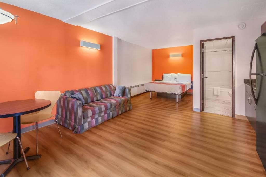 A room with a wooden floor, a sofa, a bed, and a table.