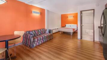 A room with a wooden floor, a sofa, a bed, and a table.