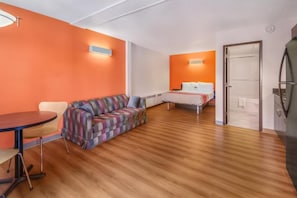 A room with a wooden floor, a sofa, a bed, and a table. - Motel 6 Lethbridge, AB (Lethbridge)