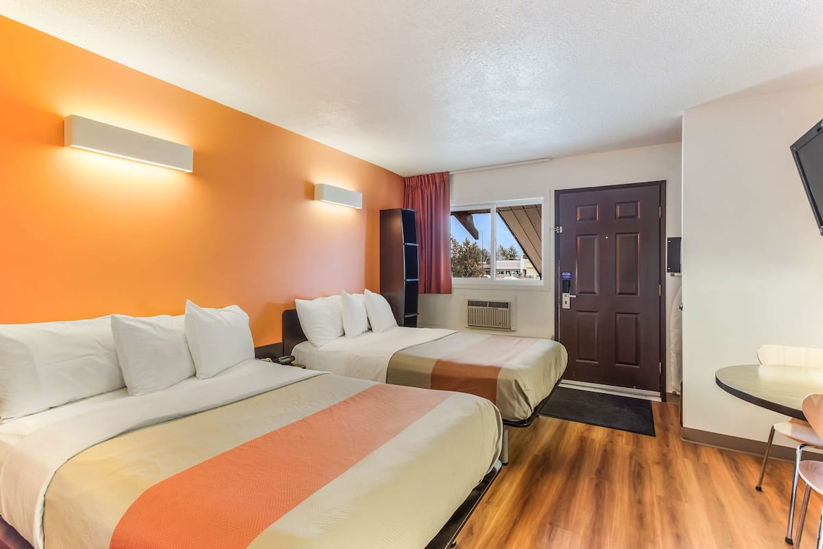Habitación de hotel con dos camas, piso de madera, una puerta y ventana con vistas.