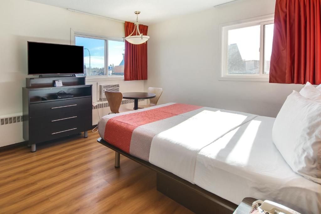 A hotel room with a bed, a desk, a chair, a television, and a window.