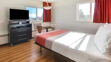 A hotel room with a bed, a desk, a chair, a television, and a window.