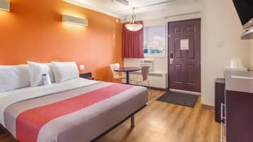 Ein Hotelzimmer mit Bett, Schreibtisch, Stuhl, kleinem Tisch und einer Tür.