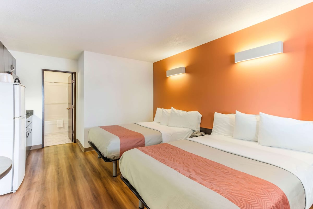 Habitación de hotel con dos camas, piso de madera, una puerta blanca y un aplique de pared.