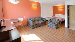 Une pièce avec un plancher en bois, un canapé, une chaise, une petite table et un lit.