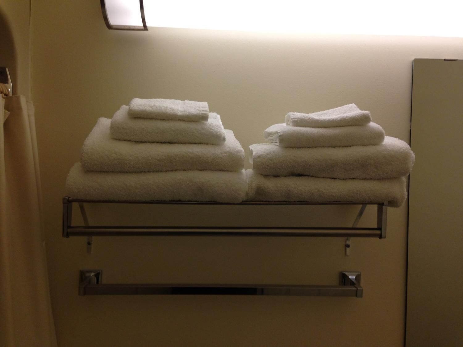 A stack of white towels on a metal rack in a room with a plain wall and a window above the rack.