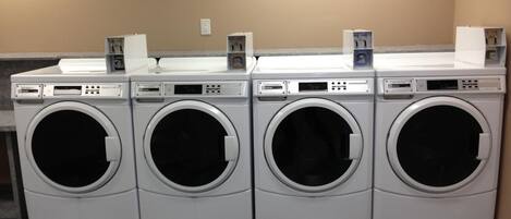 A row of four front-loading washing machines in a laundry room.