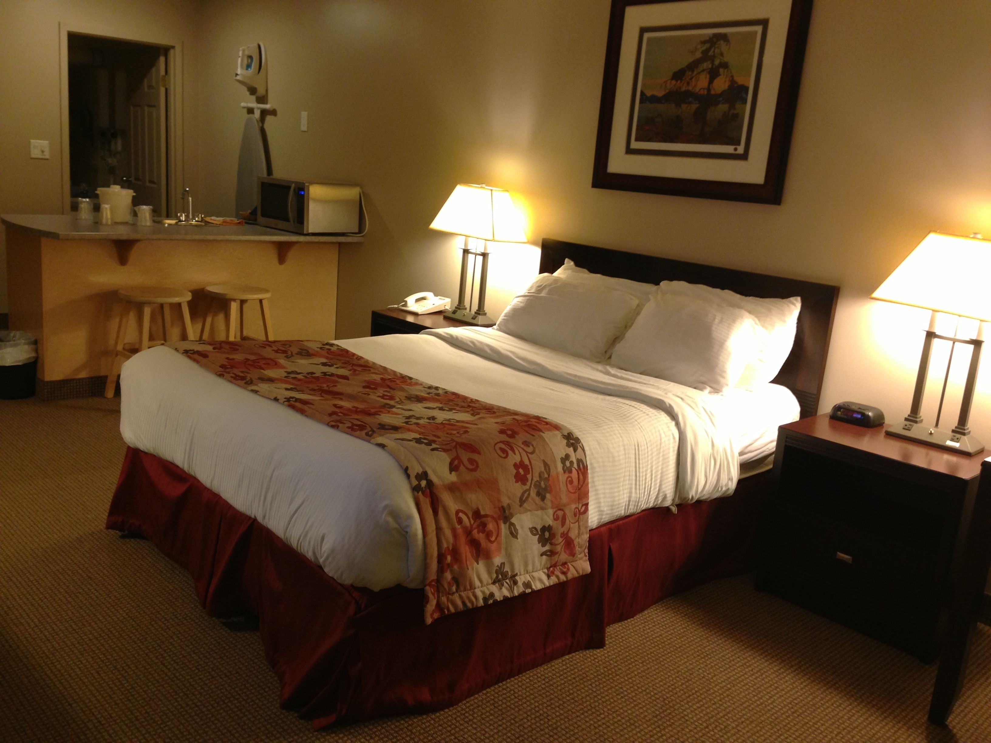 Een hotelkamer met een bed, twee bedlampen, een bureau met een telefoon, een magnetron en een stoel.