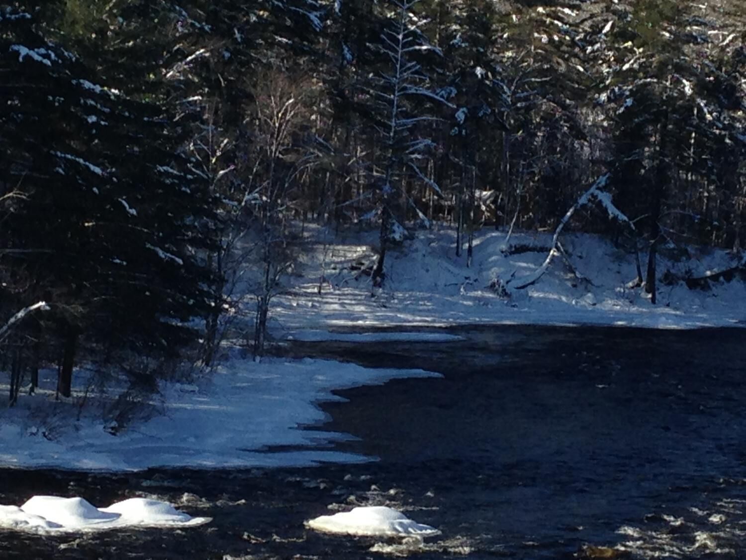 A snowy landscape with a river, trees, and a clear sky.