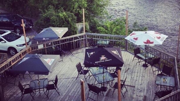 A riverside deck with outdoor seating and a view of a bridge. - Petawawa River Inn and Suites (Petawawa)