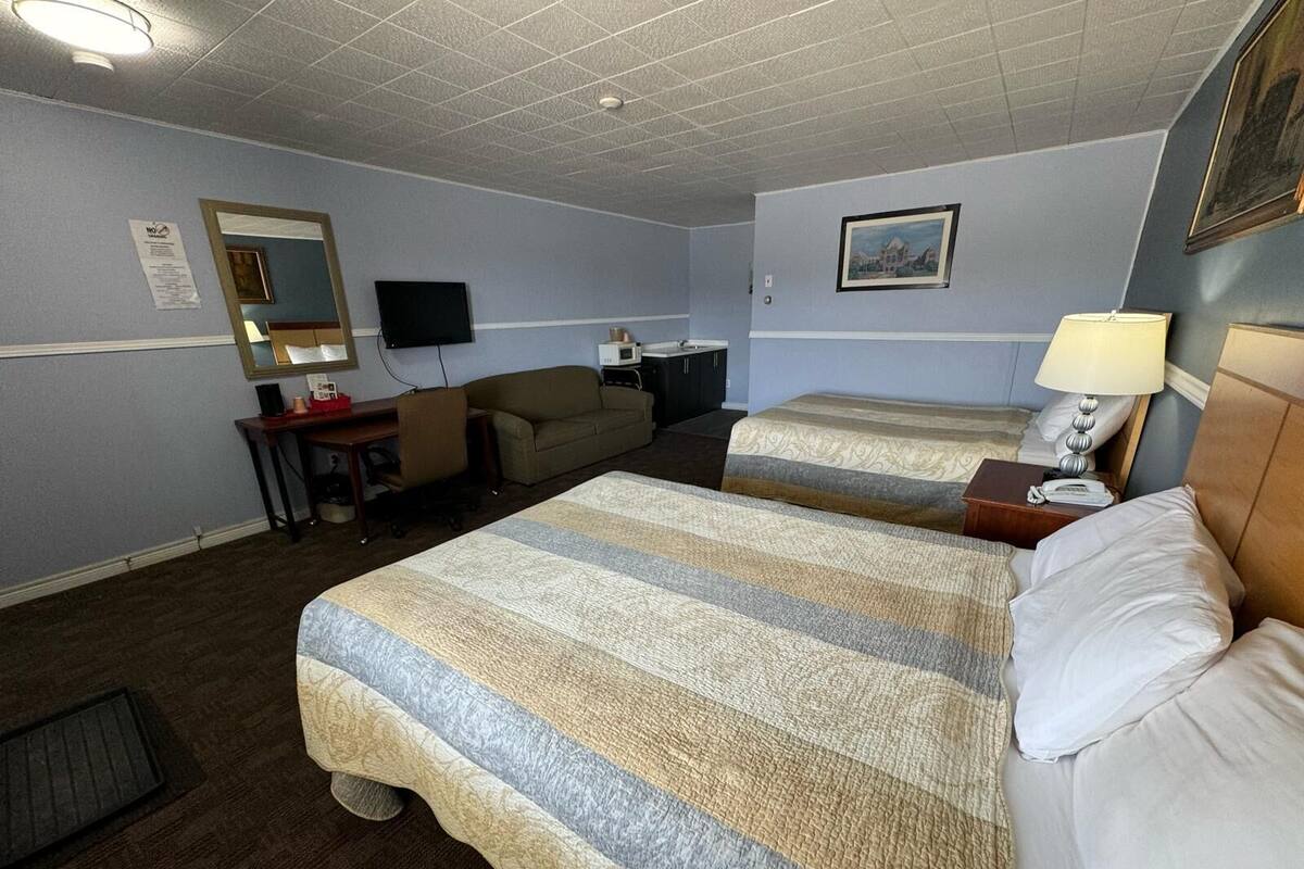 A hotel room with two beds, a desk, a chair, a television, and a painting on the wall.