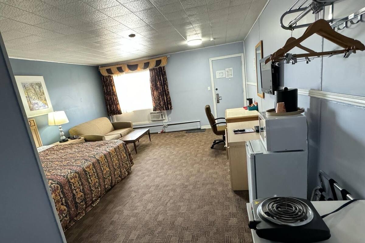 A compact hotel room with a bed, a desk, a chair, and a kitchenette.