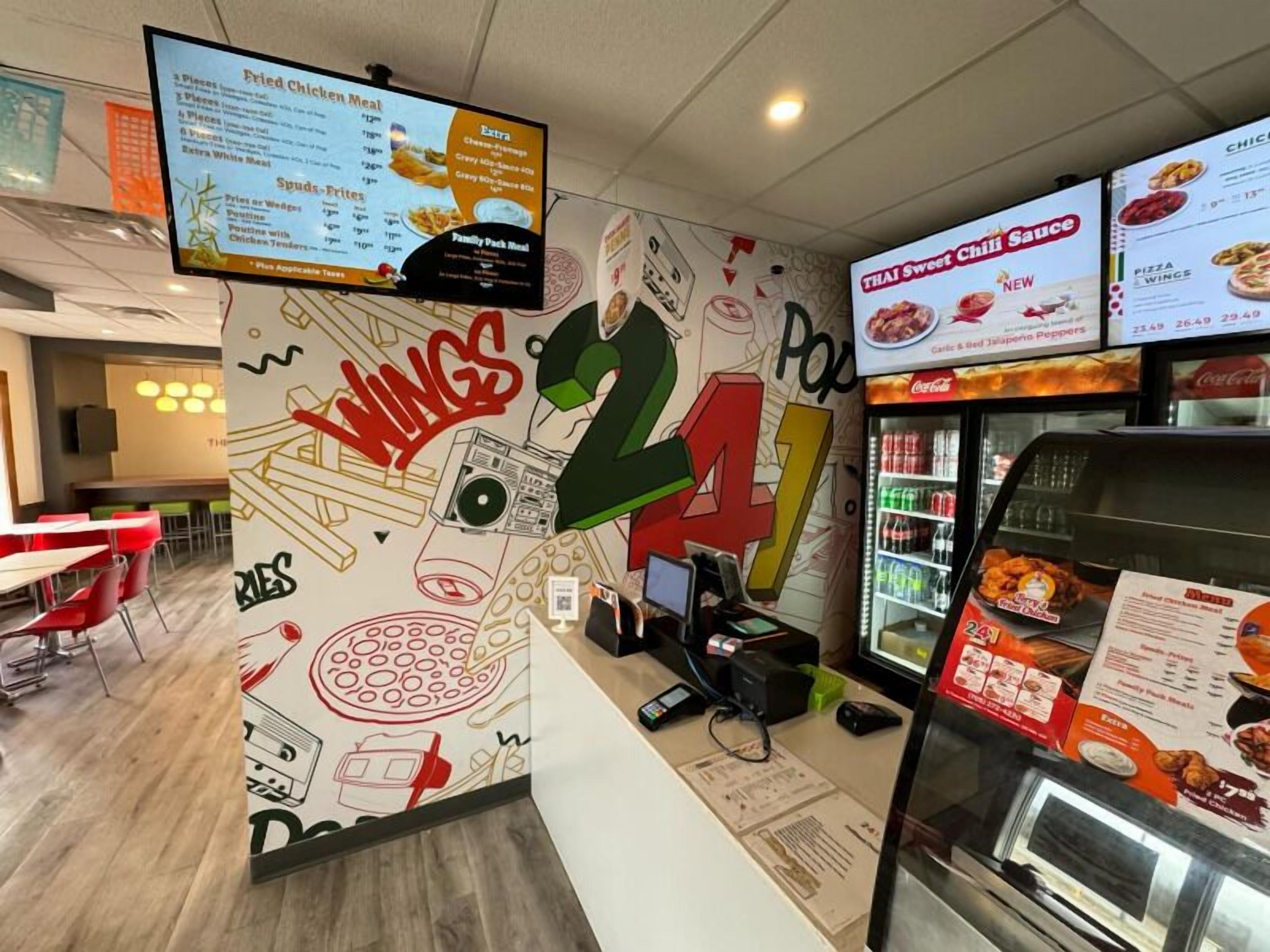 Interior de un restaurante de comida rápida con un menú en una pizarra, una pared con ilustraciones de comida y una zona de mostrador.