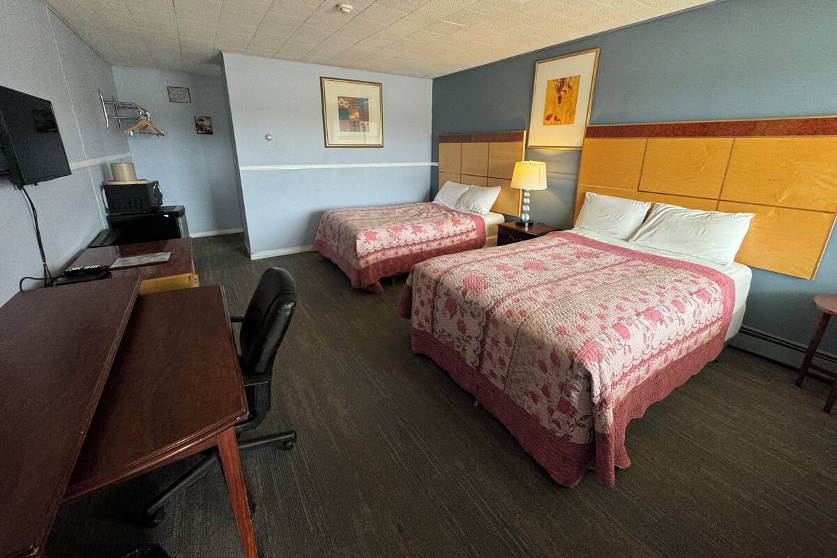 A hotel room with two beds, a desk, a chair, a TV, and a lamp.