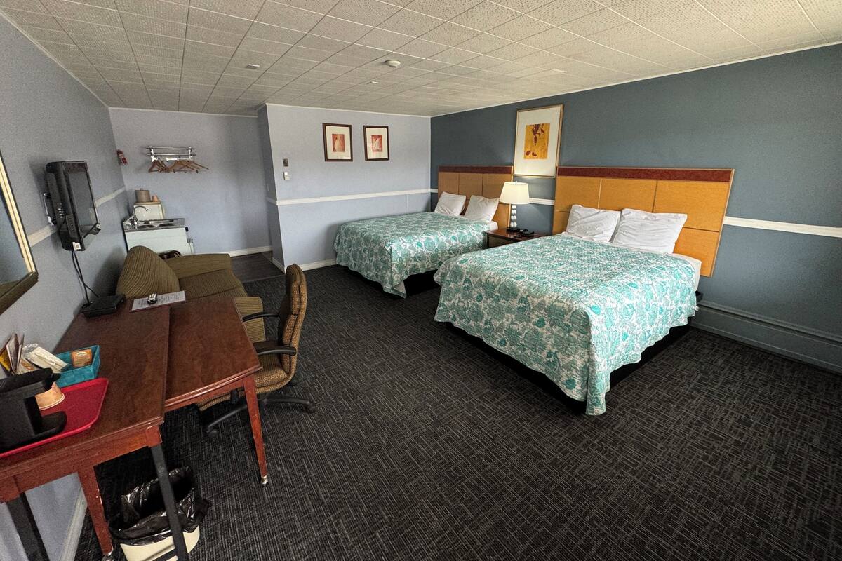 A hotel room with two beds, a desk, a chair, a TV, and a small table with a lamp.