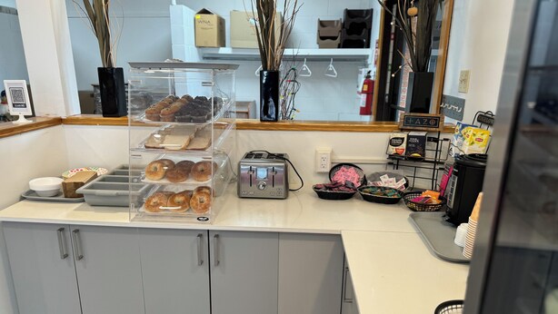 Mostrador de panadería con diversos productos horneados exhibidos en recipientes transparentes, un tostador y cestas de pastelería.