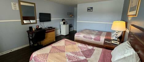 Une chambre d’hôtel avec deux lits, un bureau, une télévision, une commode et un petit réfrigérateur.