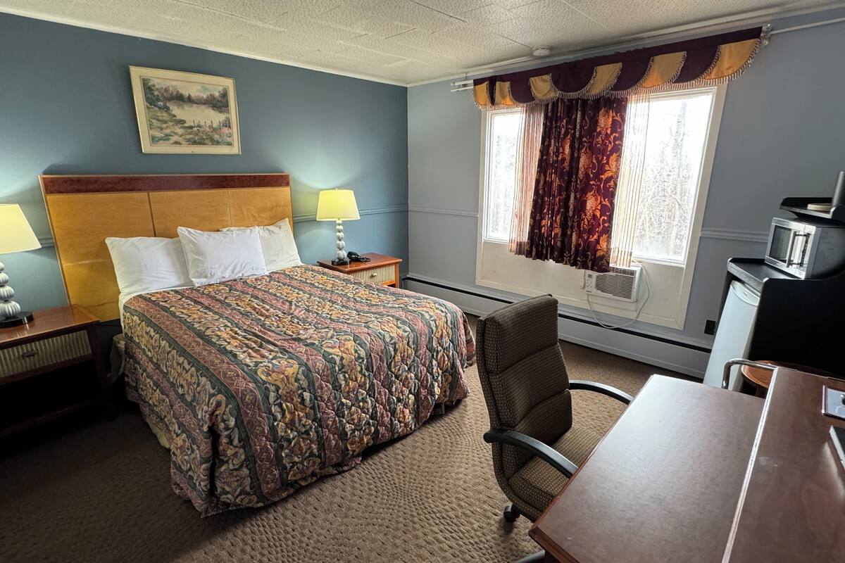 A hotel room with a large bed, a desk, a chair, a lamp, a painting on the wall, and a window with curtains.