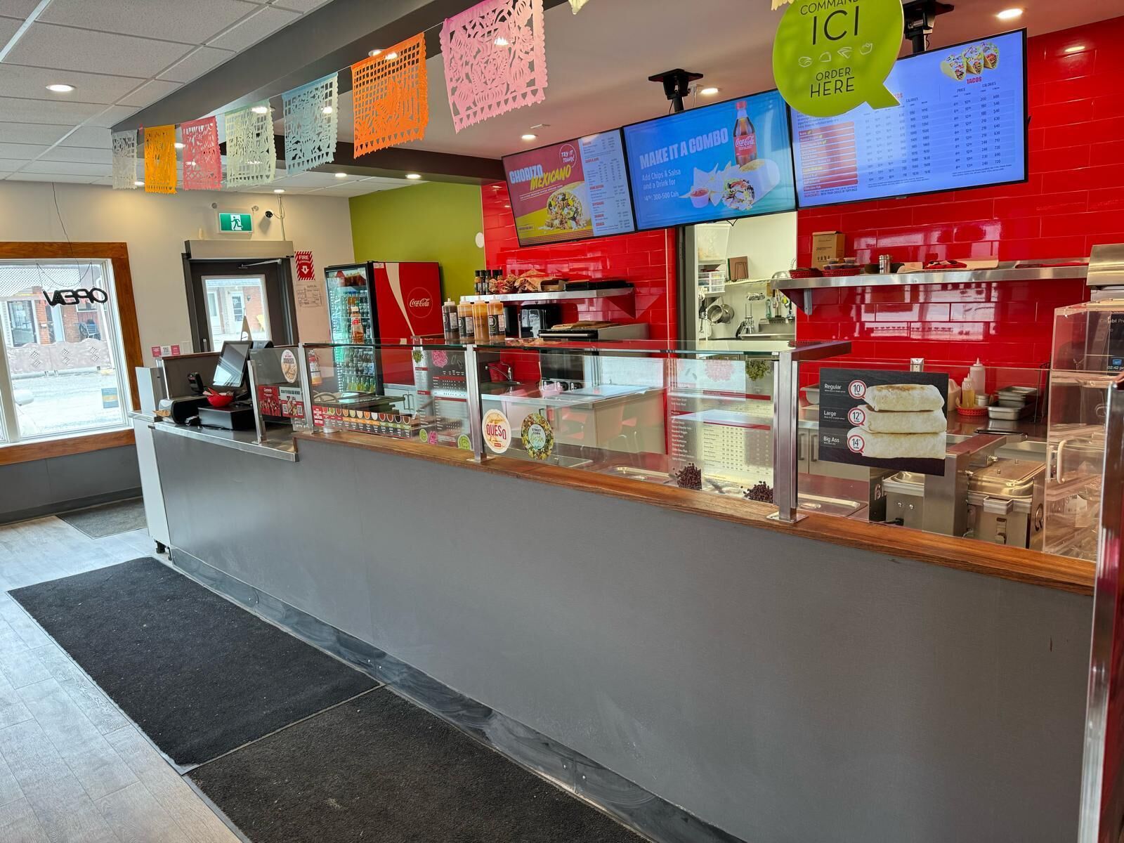 A food service counter with a menu display, a Coca-Cola refrigerator, and a glass partition.