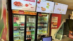 Un restaurante de comida rápida con un menú, dos refrigeradores llenos de refrescos y una caja registradora.