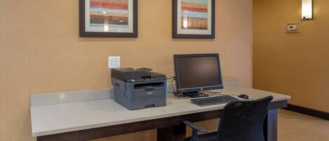 A hotel office with a desk, computer, printer, and two framed pictures on the wall.