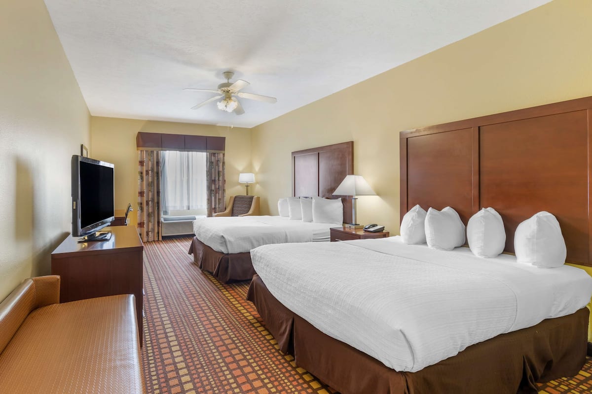 A hotel room with two beds, a TV, a desk, and a ceiling fan.